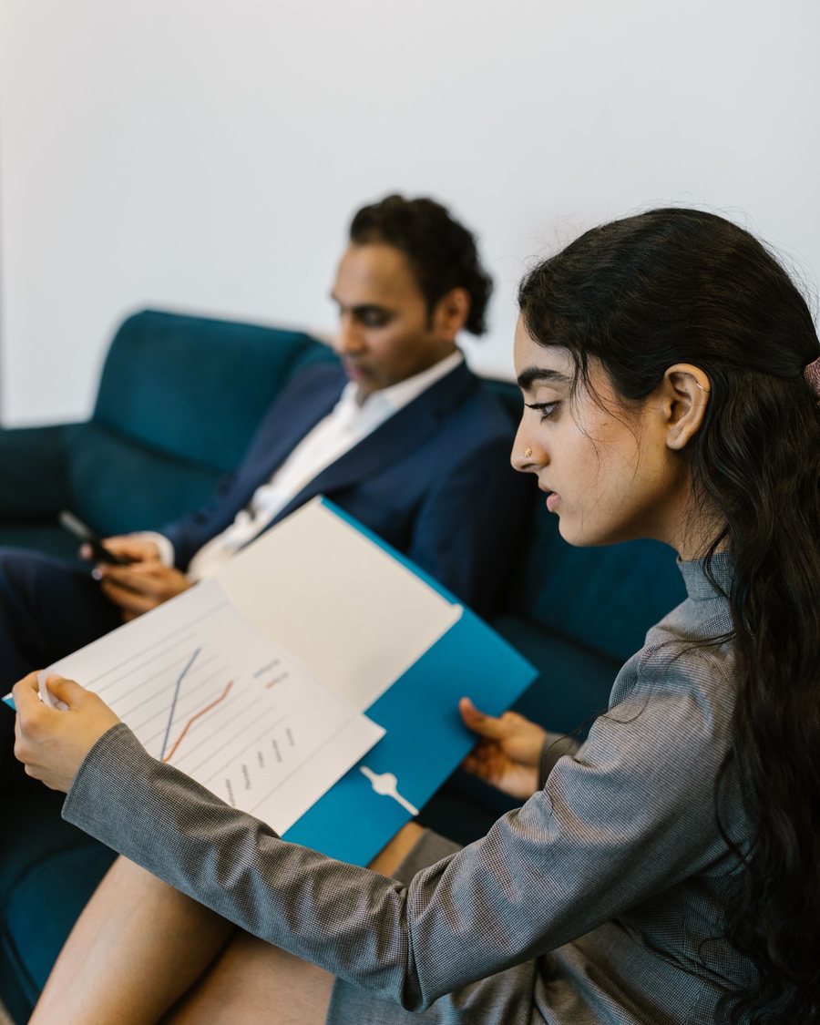 A young woman reviewing a progress chart in a folder while a colleague sits beside her
